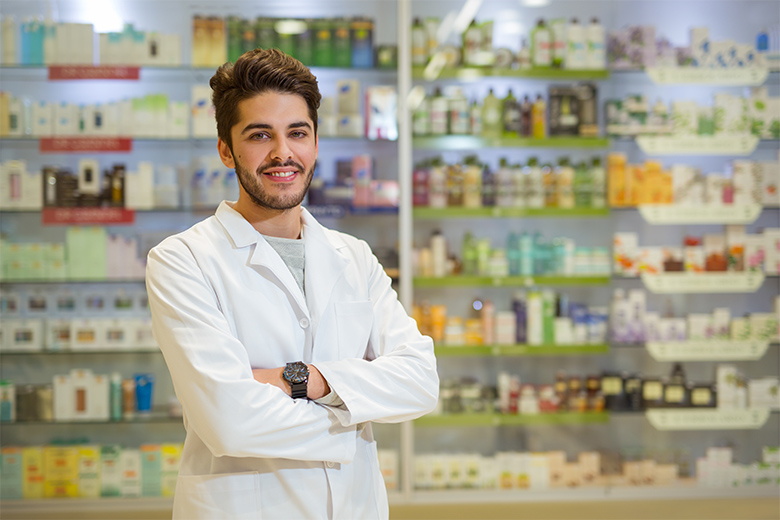 pharmacy technician standing in a pharmacy in front of a shelf of medication