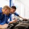 Mechanic and automotive service manager in Texas survey a car engine to diagnose the issue.