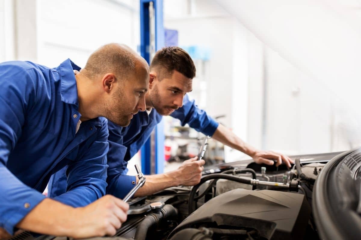 Mechanic and automotive service manager in Texas survey a car engine to diagnose the issue.