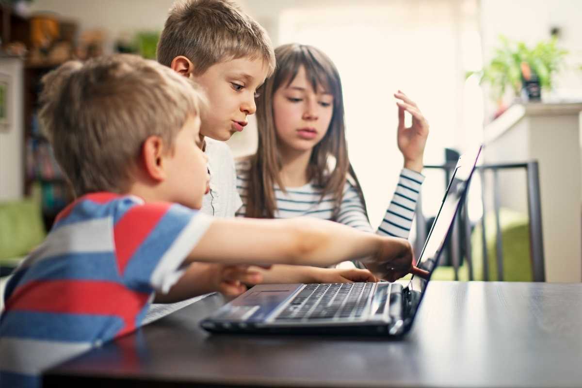 Three children looking at their laptop while talking about coding classes for kids.
