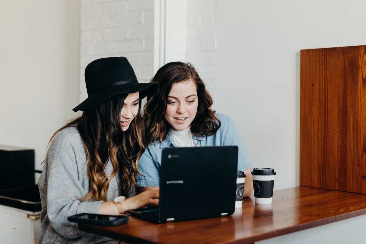 Two women sitting near laptop looking at the screen together, possibly learning SQL.