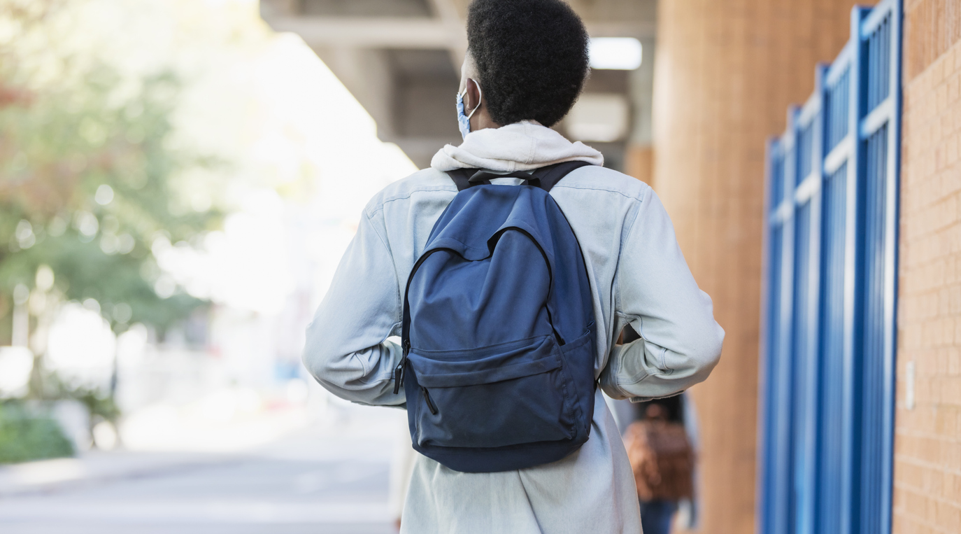 Rear View shot of a young man walking to increase mental health as he returns to school.