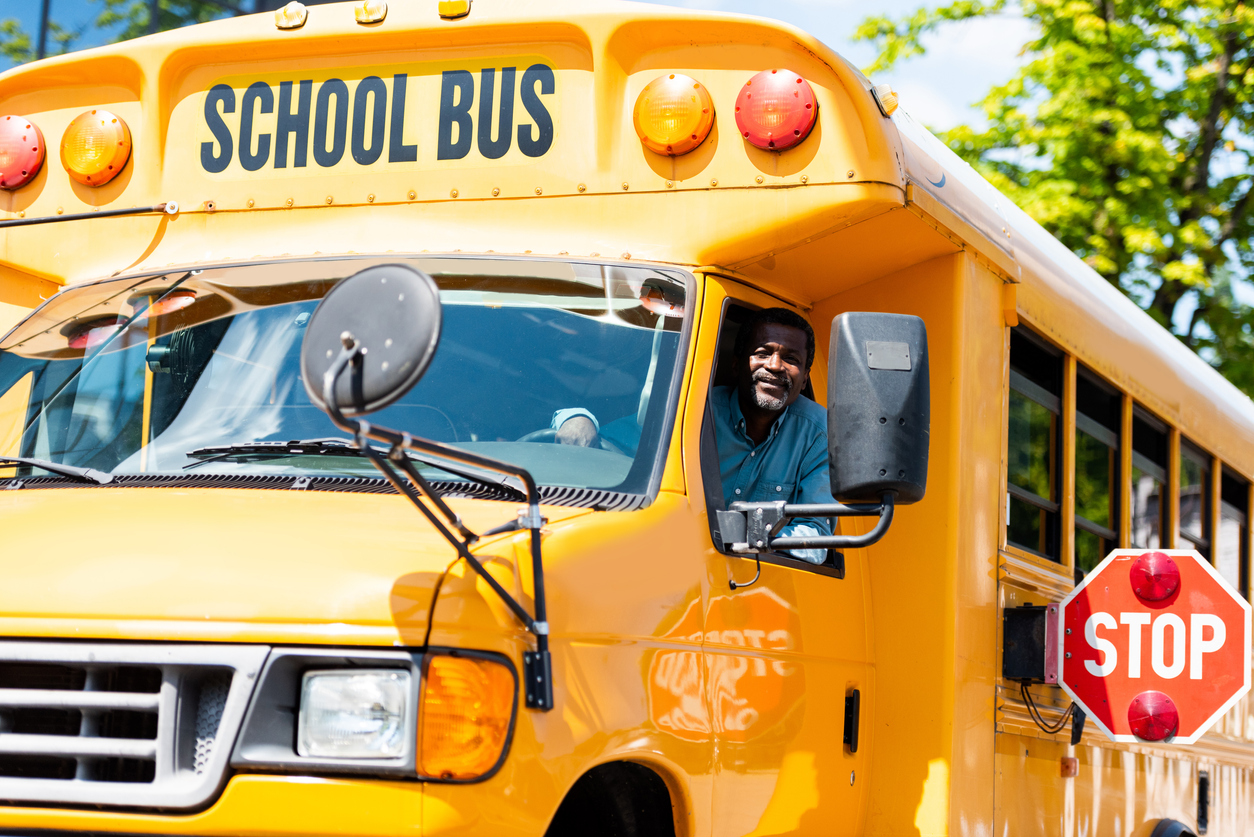 A portrait of a school bus driver sitting in his vehicle, smiling at the camera.