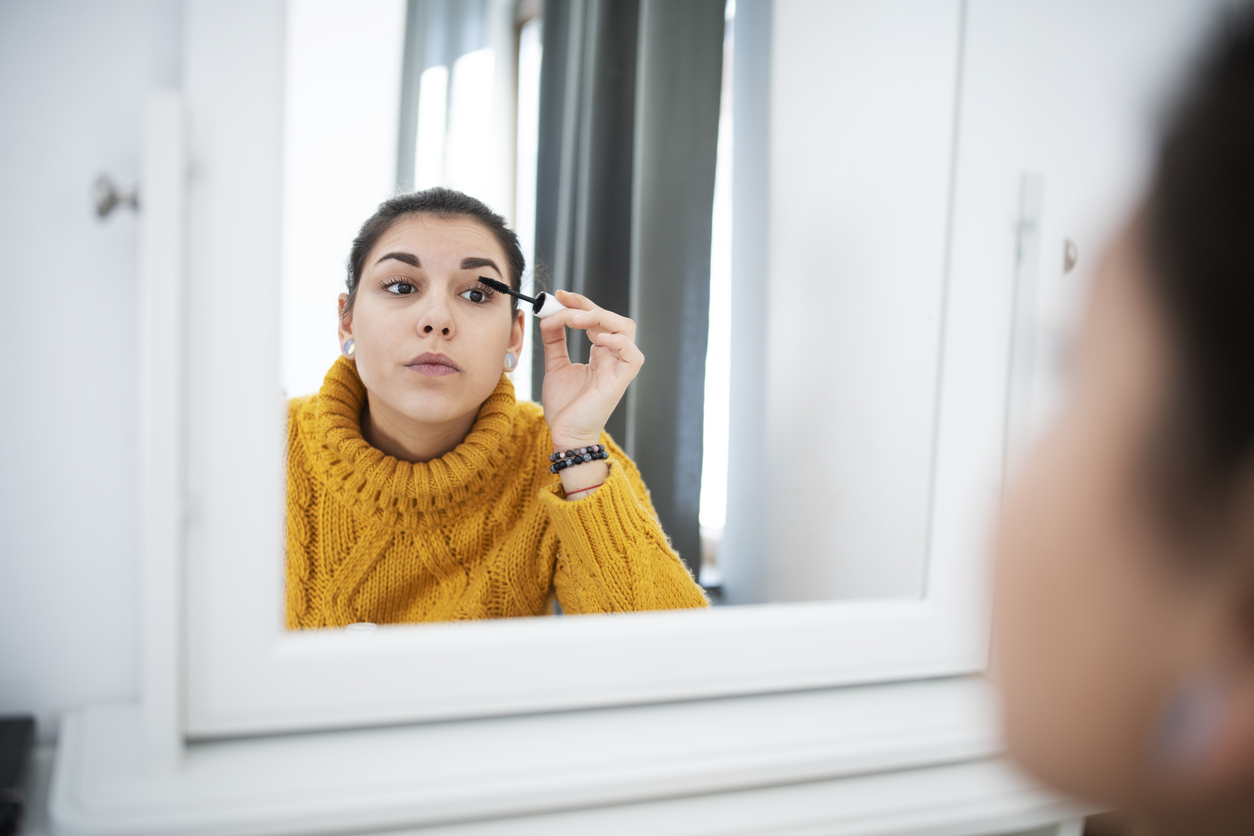 A woman applying eye makeup in the mirror before going out.