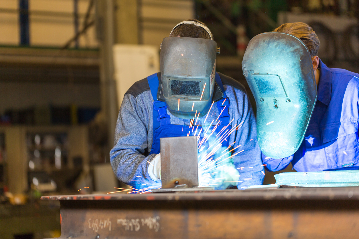 Two steel construction workers welding metal in a workshop